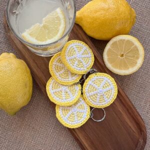 Hand-crocheted lemon keychain on wooden tray with fresh lemons — The Italian Stitch