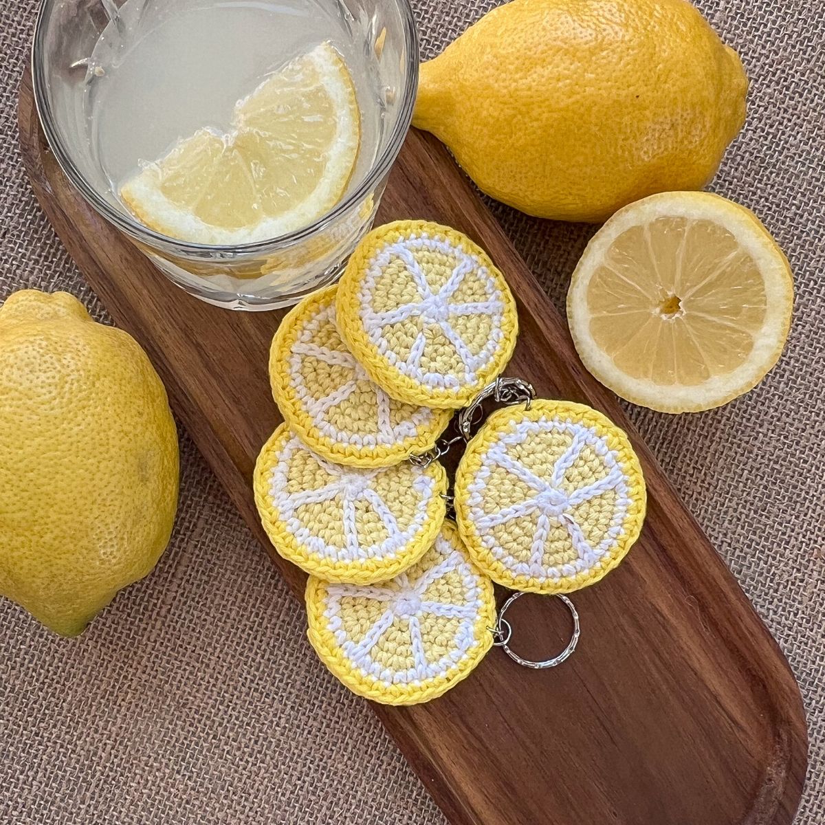 Hand-crocheted lemon keychain on wooden tray with fresh lemons — The Italian Stitch